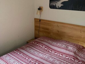 A bed with a patterned blanket, a wooden headboard, and a wall-mounted lamp.