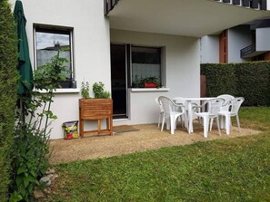 A patio with a table and chairs, a wooden planter, and a window with a view.