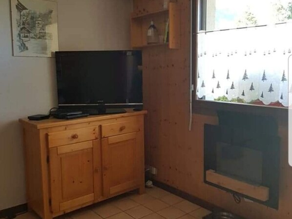 A room with a wooden cabinet, a television, and a window with a view of trees.