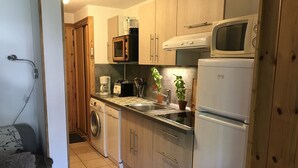 A compact kitchen with wooden cabinets, a washing machine, a microwave, and a refrigerator.