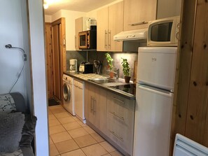 A compact kitchen with wooden cabinets, a washing machine, a microwave, and a refrigerator. - Charming apartment with WiFi in Samoëns (Samoëns)