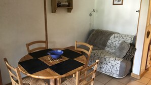 A dining area with a round wooden table, four chairs, a blue bowl, and a small wooden shelf with a basket.