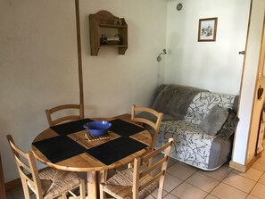Un coin repas comprenant une table ronde en bois, quatre chaises, un bol bleu et une petite étagère en bois sur laquelle se trouve un panier.