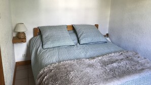 A bedroom with a bed, wooden headboard, patterned bedding, a lamp, and a fluffy rug.