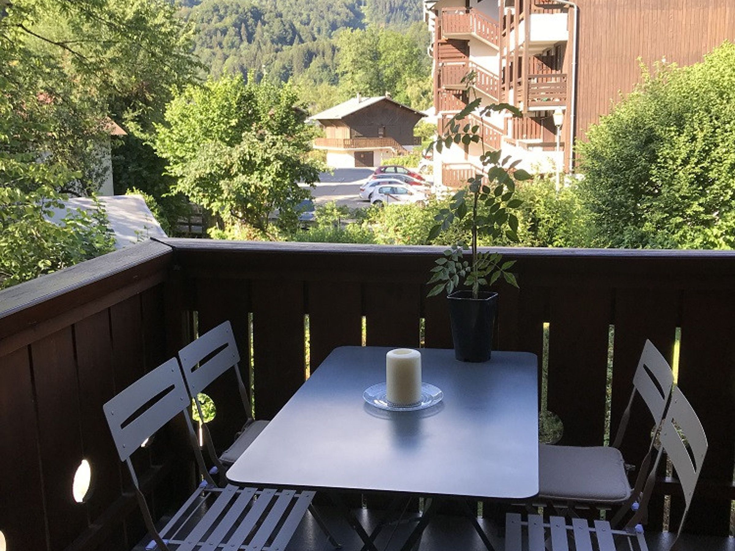 A balcony with a table and chairs, a potted plant, and a candle.