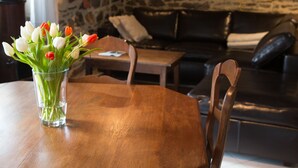 A dining area with a wooden table and chairs, a vase of tulips, and a stone wall in the background. - Detached house with terrace, pellet stove and peaceful garden. (Canisy)