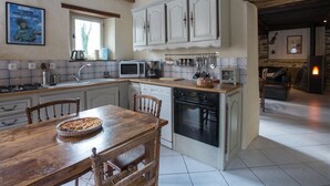 A kitchen with wooden beams, white cabinets, a dining table with chairs, a microwave, and a stove. - Detached house with terrace, pellet stove and peaceful garden. (Canisy)