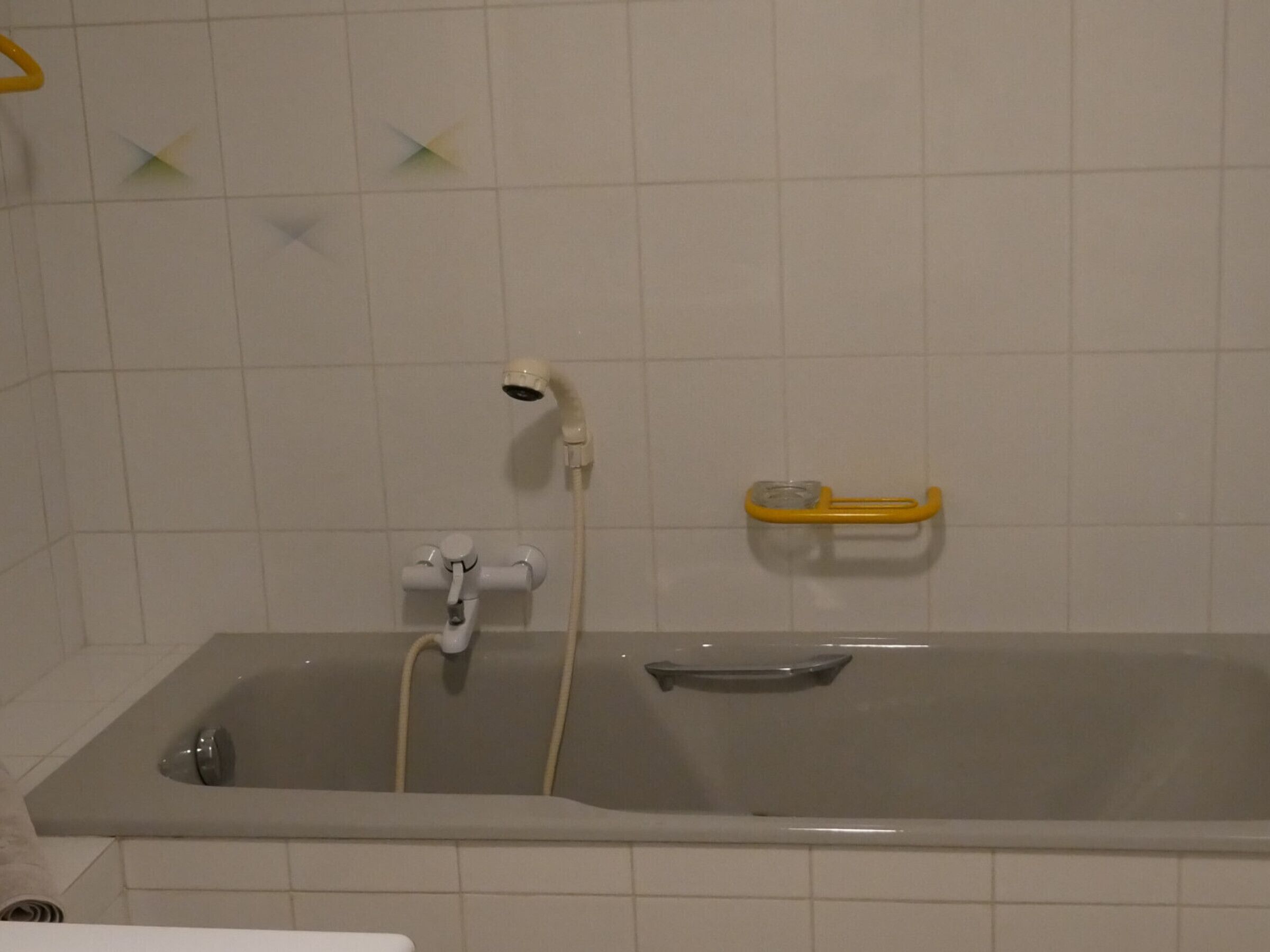 Un bany amb banyera, test de dutxa i un plat de sabó groc a la paret.