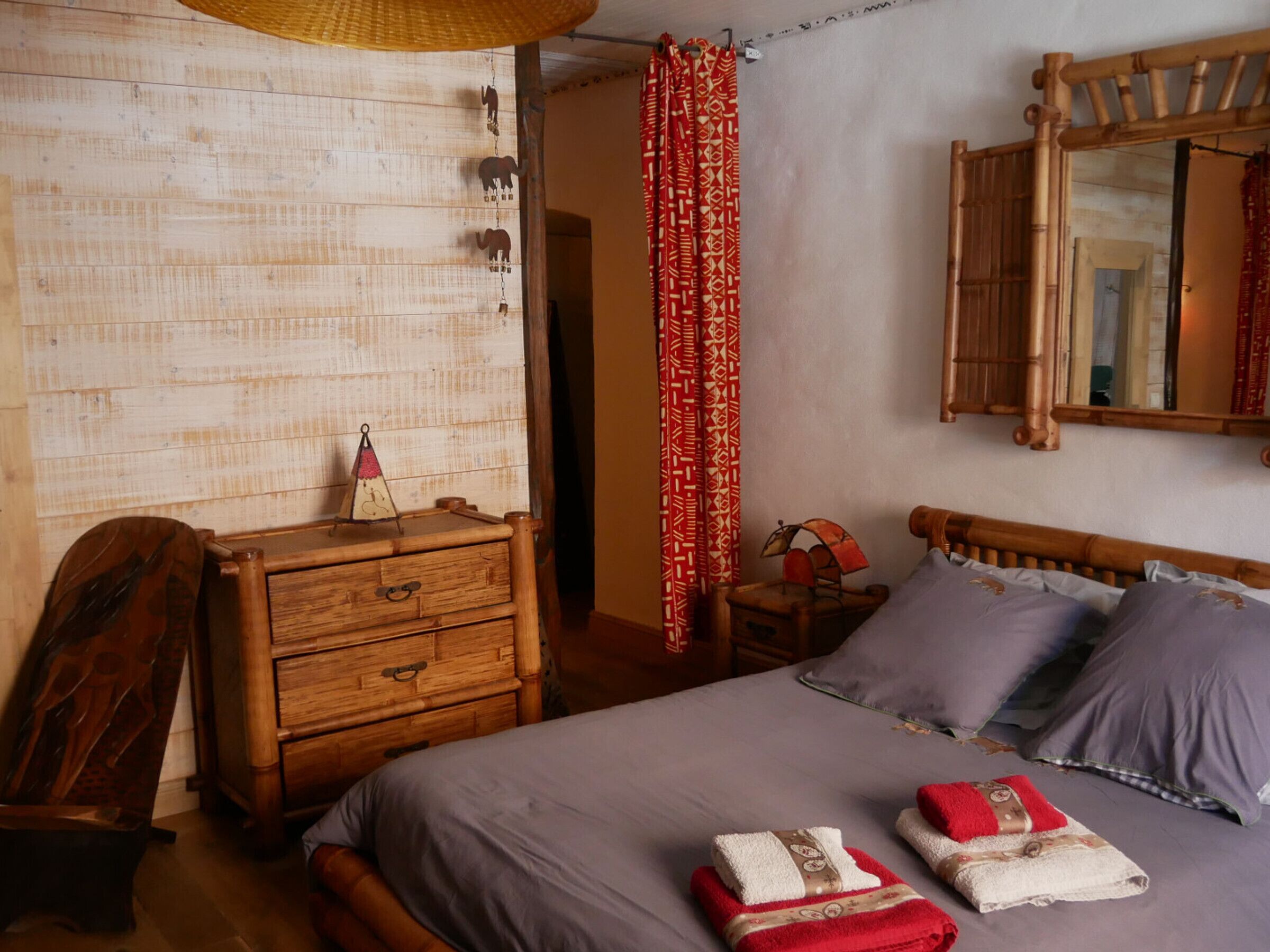 A bedroom with a wooden dresser, a bed with grey bedding, and a mirror on the wall.