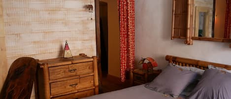 A bedroom with a wooden dresser, a bed with grey bedding, and a mirror on the wall.