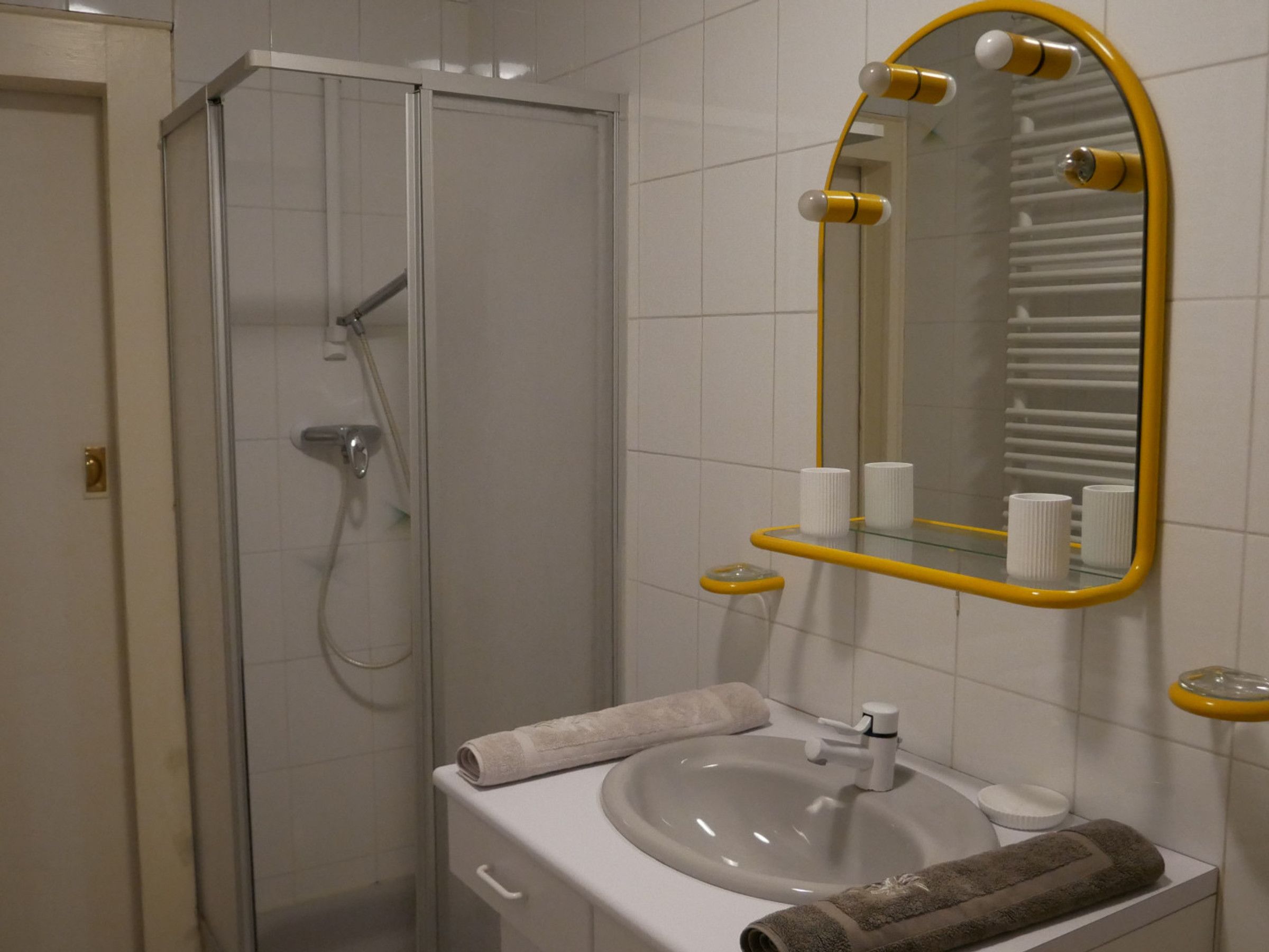 Un baño con ducha envuelta en vidrio, un lavabo con espejo y artículos de aseo en un estante.