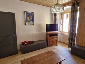 A living room with a wooden table, a sofa, a TV on a wooden stand, and a poster on the wall. - Spacious apartment in Samoëns, 3 bedrooms, WiFi, 10 people (Samoëns)