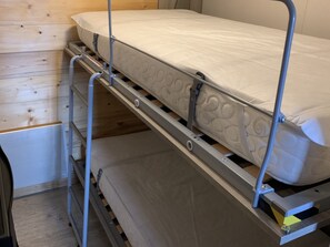 A bunk bed with a mattress and metal frame, wooden flooring, and a metal ladder.
