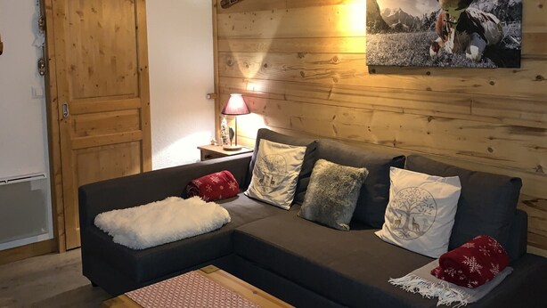 Ein gemütliches Wohnzimmer mit einer Holzwand, einer Couch mit gemusterten Kissen, einer Lampe und einem gerahmten Bild.