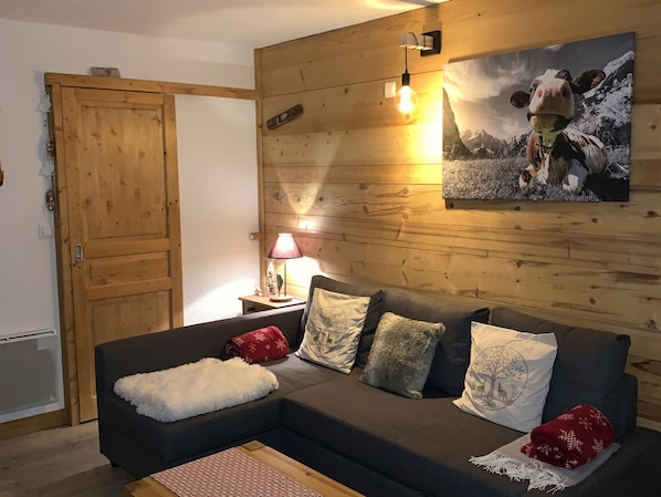 A cozy living room with a wooden wall, a sofa with patterned cushions, a lamp, and a framed picture.