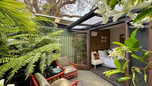 A cozy outdoor seating area with wicker chairs and a table, surrounded by lush greenery and white flowers.