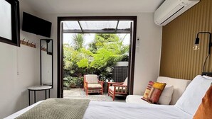 A bedroom with a bed, a sofa, a chair, and a small table. There is a window with a view of greenery outside.