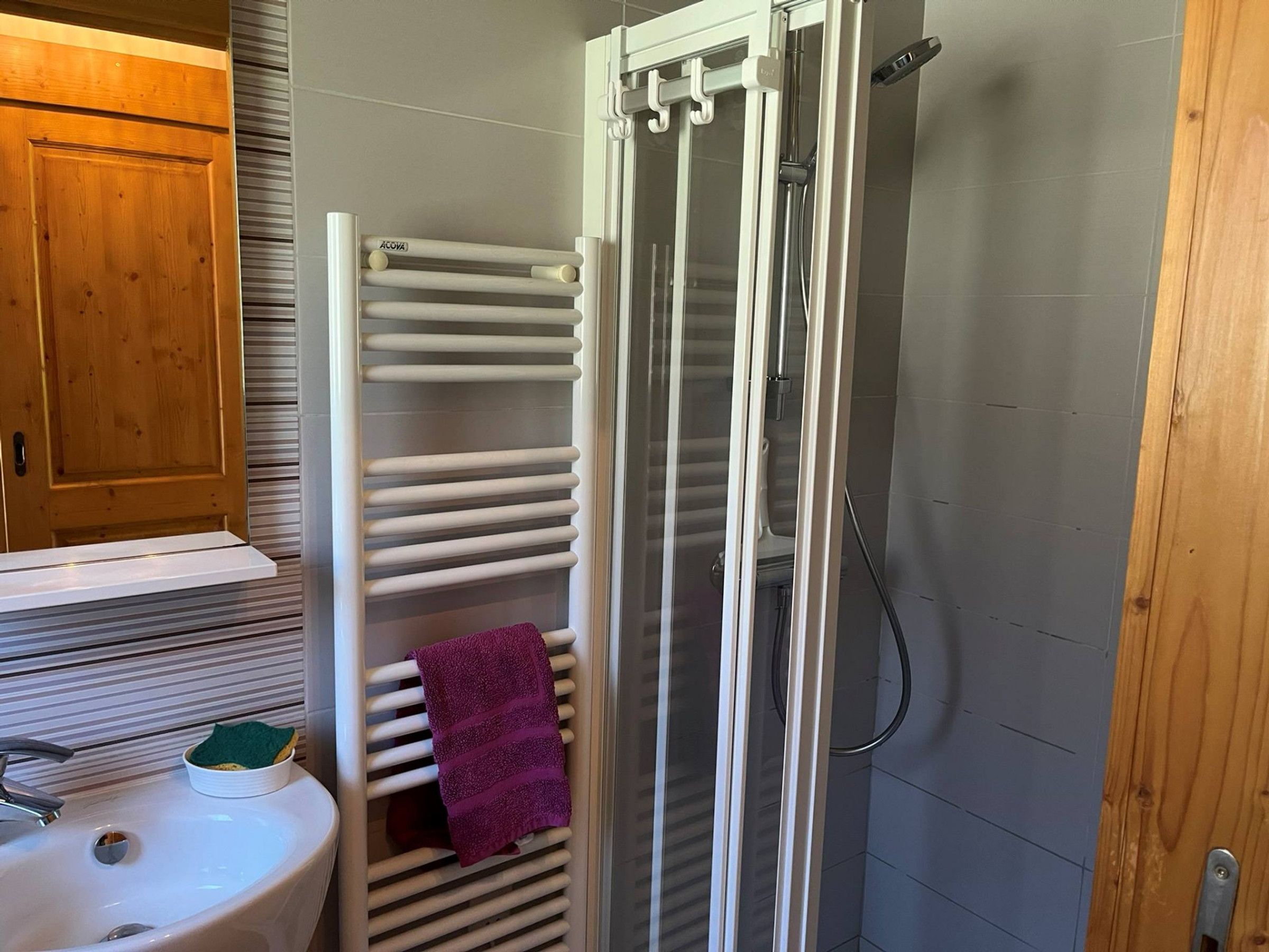 A bathroom with a white sink, a wooden cabinet, a glass shower enclosure, and a towel rack with a purple towel.