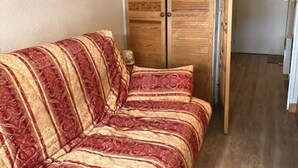 A room with a wooden wardrobe, a sofa with a patterned cover, and a wooden floor.