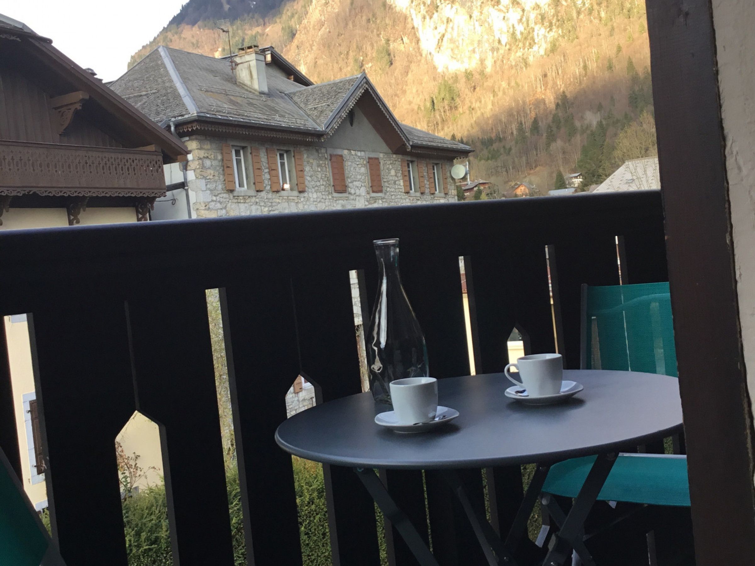 Un balcon avec une table et des chaises, donnant sur une région montagneuse parsemée de bâtiments traditionnels.