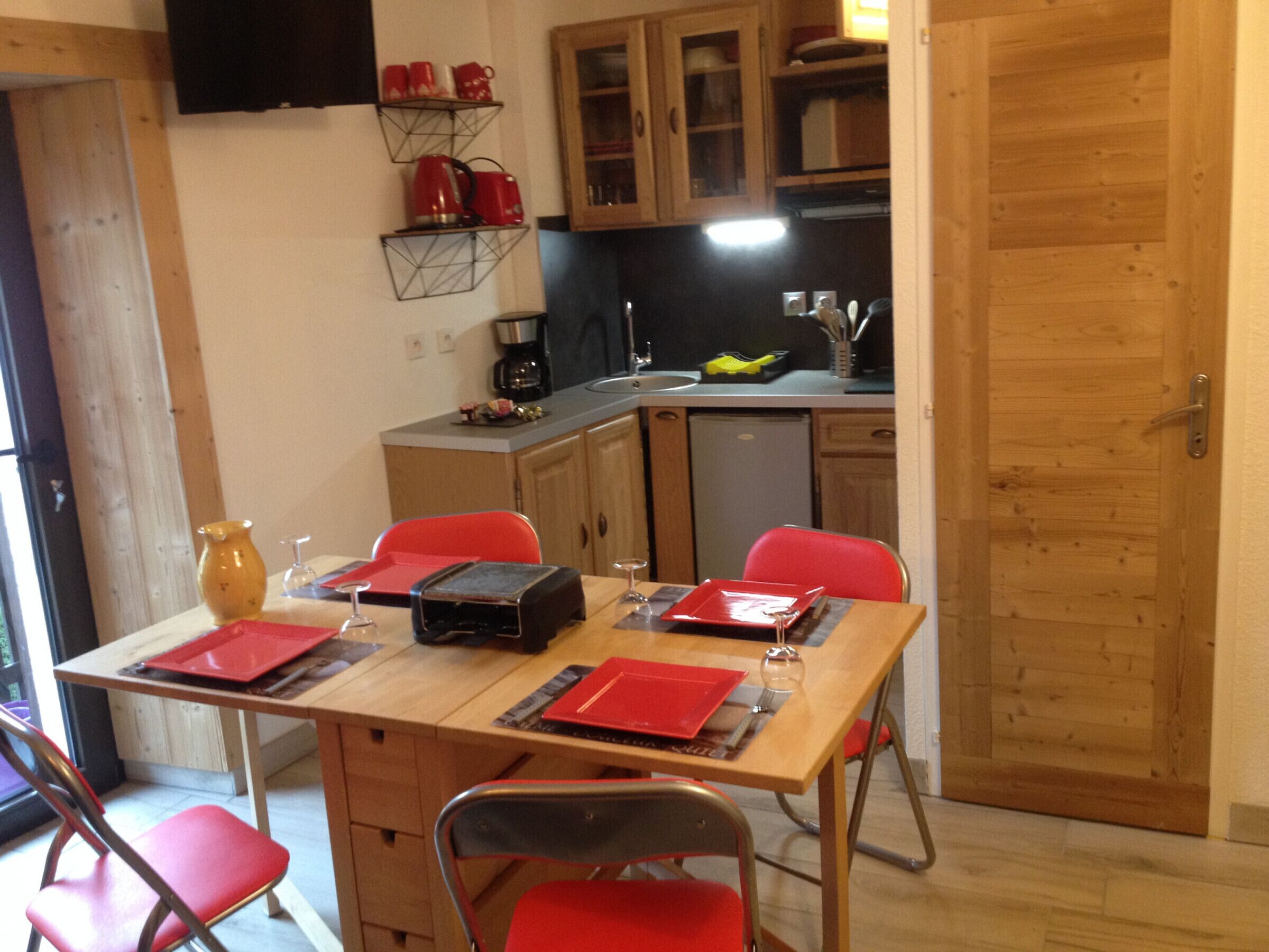 Een eetgedeelte met een tafel voor vier personen, stoelen, een koffieapparaat en een keuken op de achtergrond.