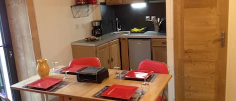 A dining area with a table set for four, chairs, a coffee machine, and a kitchen in the background.