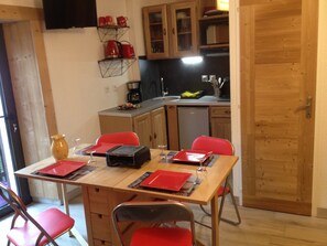 A dining area with a table set for four, chairs, a coffee machine, and a kitchen in the background. - Cozy studio for 4 in Samoëns (Samoëns)