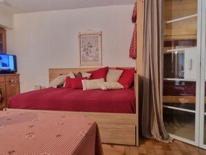 Un dormitorio con cama, televisión, un cuadro enmarcado en la pared y una puerta corrediza de vidrio.