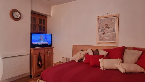 Een slaapkamer met een bed, een televisie, een houten kast, een klok en een ingelijst beeld aan de muur.