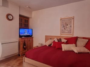 A bedroom with a bed, a television, a wooden cabinet, a clock, and a framed picture on the wall.