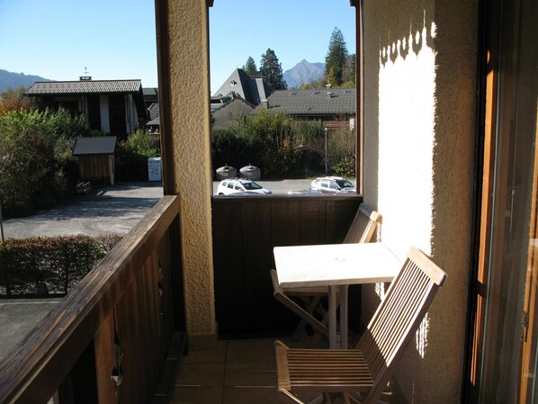 A balcony with a wooden bench and table, overlooking a parking area and buildings with a mountain in the background. - Apartment in Samoëns with Wifi, ideal for 3 pers. (Samoëns)