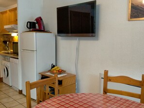 Una cocina compacta con refrigerador, microondas y una pequeña mesa con frutero.