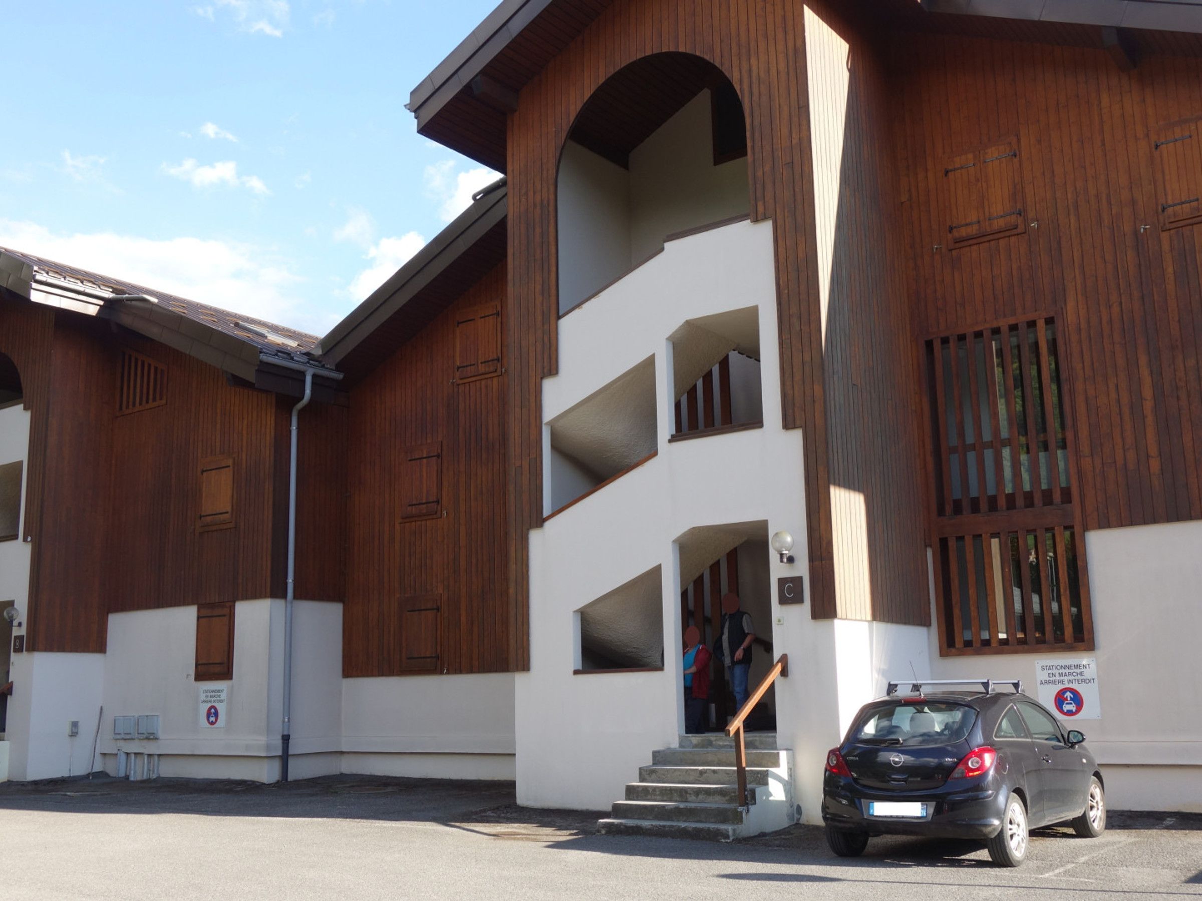 Un bâtiment à la façade blanche agrémentée d’éléments en bois, avec un escalier menant à un niveau supérieur.