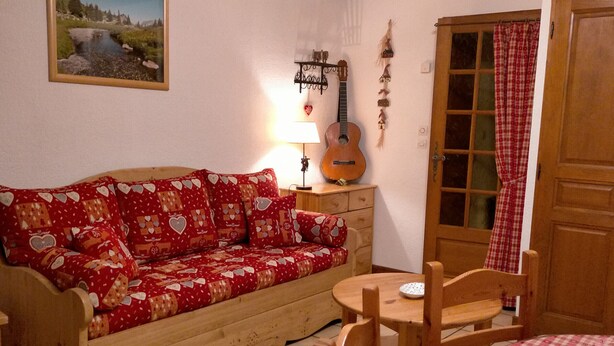 Een knus ingerichte kamer met een houten bank, een klein tafeltje en een gitaar.