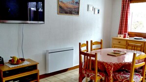 Een eetruimte met een tafel, stoelen, een televisie, een schilderij en een raam met gordijnen.
