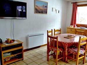 A dining area with a table, chairs, a television, a painting, and a window with curtains. - Cozy 2-room apartment with Wifi in Samoëns (Samoëns)