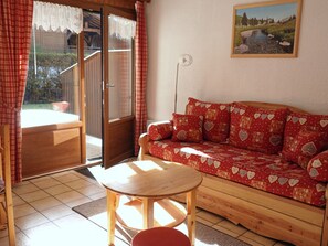 A cozy room with a wooden sofa, a small round table, and a sliding glass door leading to an outdoor area. - Cozy 2-room apartment with Wifi in Samoëns (Samoëns)