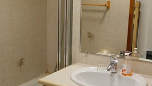 Een badkamer met een witte wastafel, een houten kastje, een spiegel en een douchehoek.