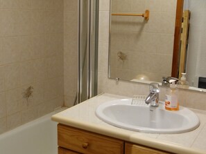 A bathroom with a white sink, a wooden cabinet, a mirror, and a shower area. - Cozy 2-room apartment with Wifi in Samoëns (Samoëns)