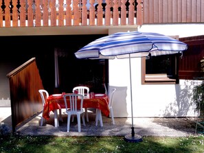 Un patio al aire libre con una mesa y sillas, un paraguas a rayas y una valla de madera.