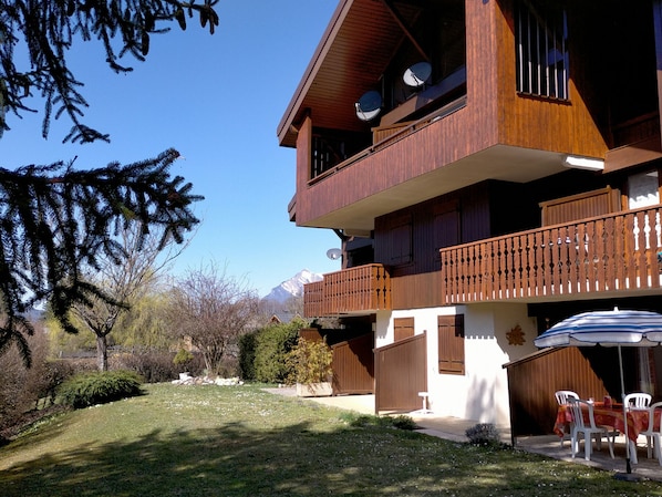 Un edificio de madera de dos pisos con balcones, un espacio de estar al aire libre cubierto y una vista de montañas al fondo.