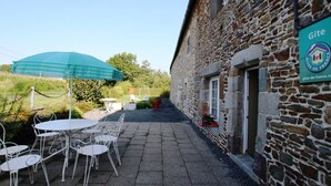 A stone building with a sign reading "Gîte" and a patio area with outdoor seating and a striped umbrella.
