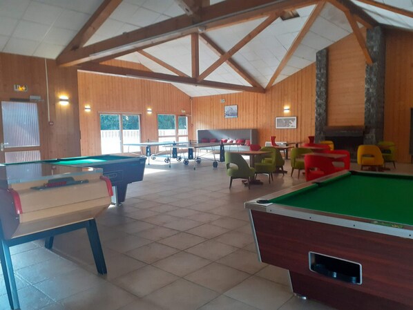 Een recreatieruimte met pooltafels, stoelen en een open haard.