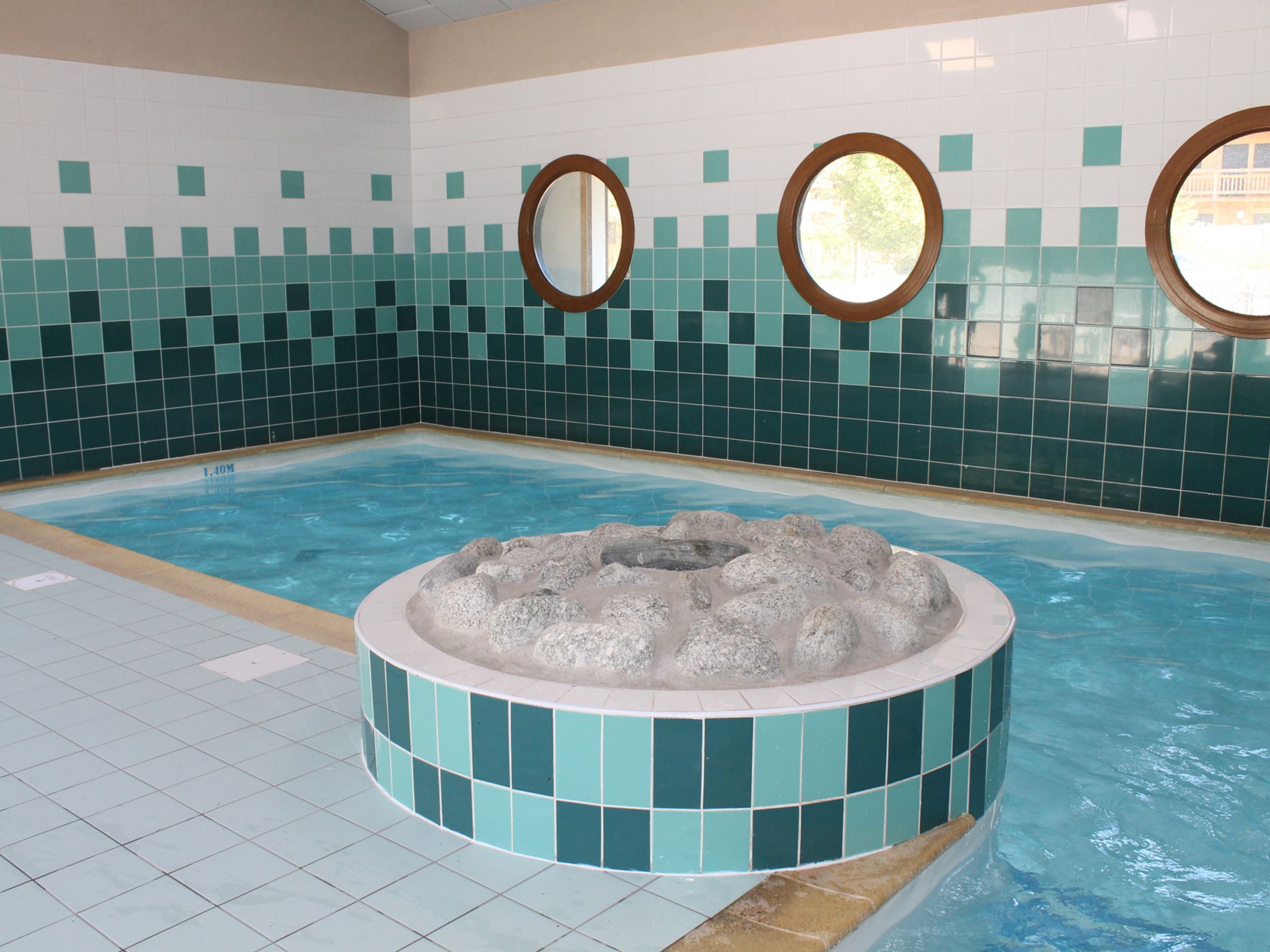 A swimming pool with a hot tub, tiled walls, and two round mirrors.