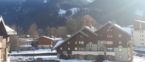 A snow-covered mountain village with traditional wooden buildings, a small bridge, and a clear view of the surrounding mountains.