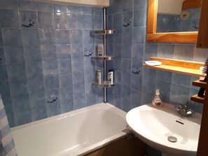 A bathroom with blue tiles, a white bathtub, a sink, and a mirror above the sink.