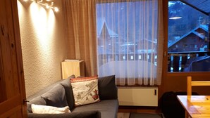Una habitación acogedora con un sofá de color oscuro, una pequeña mesa de madera y una ventana con vistas a un paisaje nevado.