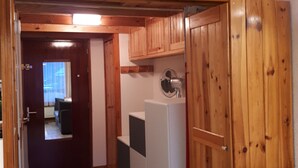 Interior de madera con una puerta que da a una habitación, un electrodoméstico blanco y un ventilador de techo.