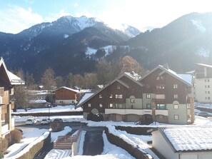 A snow-covered mountain village with traditional wooden buildings, a small bridge, and a clear view of the surrounding mountains.