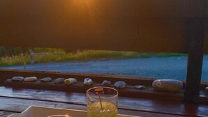 Une vue sur le coucher de soleil depuis une terrasse en bois, avec un verre posé sur la table.